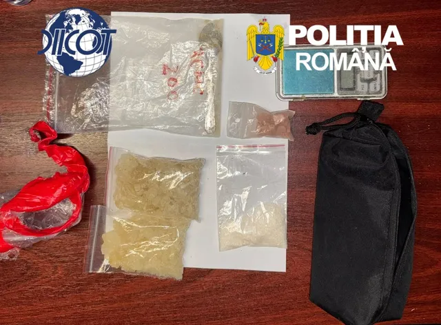 Mai multe plicuri de plastic transparente conținând substanțe solide și granulare sunt așezate pe o suprafață de culoare închisă lângă un obiect textil negru.