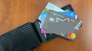 Un portofel negru deschis conține mai multe carduri bancare colorate, printre care unul de culoare gri cu logo-ul Mastercard este vizibil în partea de jos.