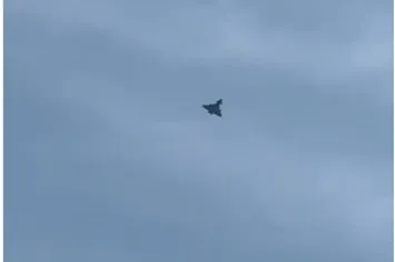 O siluetă întunecată de avion zboară pe un cer acoperit de nori gri.