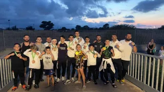 Un grup de sportivi stă în linie, purtând medalii și echipamente sportive, sub un cer de seară.