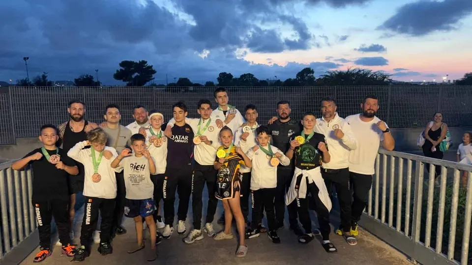 Un grup de sportivi stă în linie, purtând medalii și echipamente sportive, sub un cer de seară.