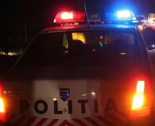 Spatele unei mașini de poliție cu girofaruri aprinse roșu și albastru este vizibil pe un fundal întunecat.