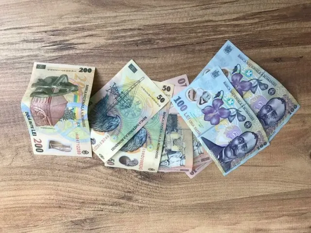 Mai multe bancnote românești de diferite valori sunt întinse pe o suprafață de lemn maro.