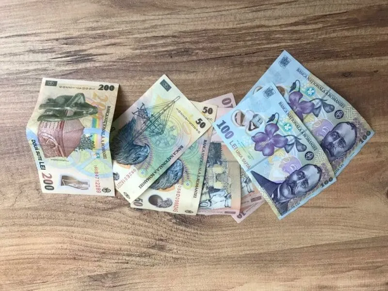 Mai multe bancnote românești de diferite valori sunt întinse pe o suprafață de lemn maro.