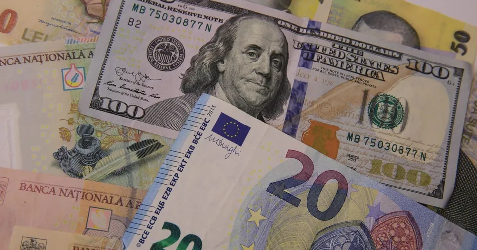 Diverse bancnote de euro, dolar și leu sunt întinse pe o suprafață, printre care se observă un portret de pe o bancnotă de o sută de dolari.