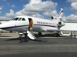 Un avion privat alb cu dungi roșii și albastre este parcat pe o pistă sub un cer cu nori plutind.