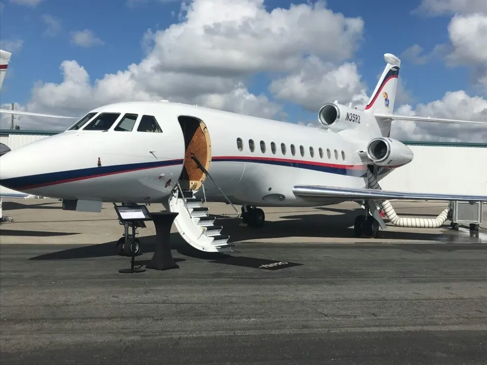 Un avion privat alb cu dungi roșii și albastre este parcat pe o pistă sub un cer cu nori plutind.