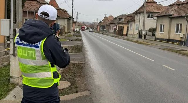 Un polițist cu vestă reflectorizantă galbenă și șapcă albă stă pe marginea unui drum asfaltat lângă o clădire.
