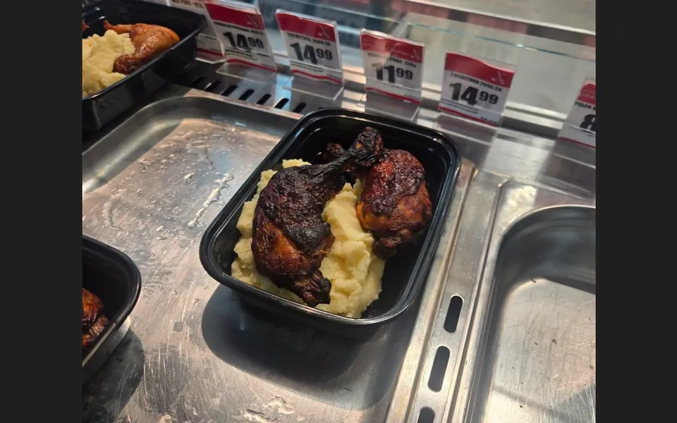 Două porții de pui gătit cu garnitură de cartofi zdrobiți sunt prezentate în recipiente negre pe o suprafață metalică de prezentare.