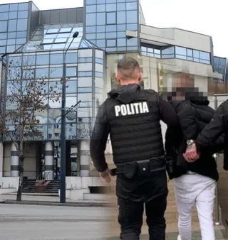 Un polițist în uniformă neagră cu inscripția POLITIA pe spate conduce un individ cu mâinile în spate în fața unei clădiri cu fațadă de sticlă.