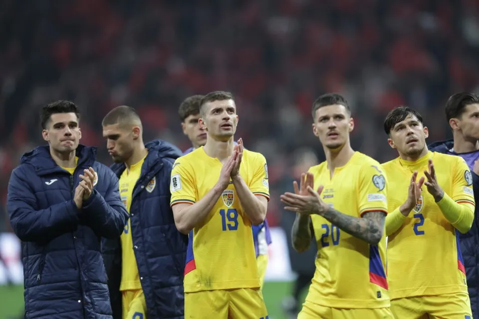 Un grup de bărbați îmbrăcați în echipamente sportive galbene și jachete albastre stau în picioare pe un teren de fotbal.