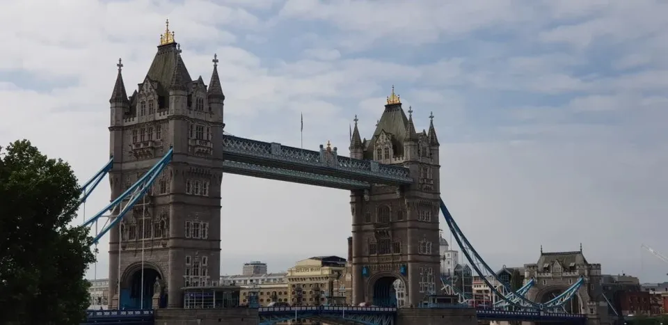 Podul Tower Bridge se ridică peste un râu sub un cer parțial înzăpezit, cu clădiri urbane vizibile în fundal.