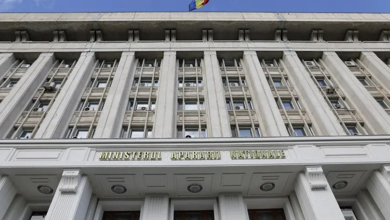 Fațada unei clădiri înalte de culoare gri cu numeroase ferestre și un steag deasupra acoperișului.