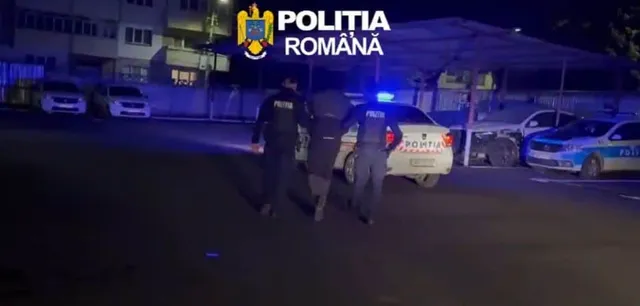 Trei polițiști stau lângă o mașină de serviciu cu girofaruri aprinse pe un drum asfaltat noaptea.