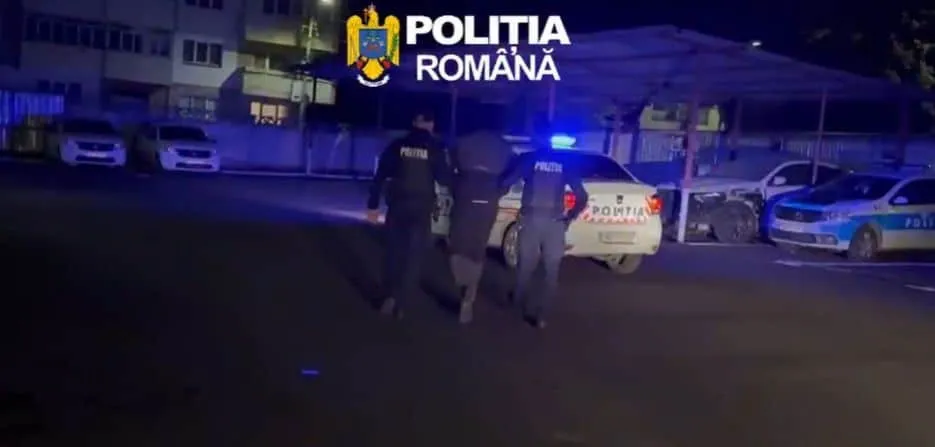 Trei polițiști stau lângă o mașină de serviciu cu girofaruri aprinse pe un drum asfaltat noaptea.