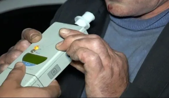 Două mâini țin un aparat de testare alcoolemică cu un dispozitiv de suflare alb deasupra.