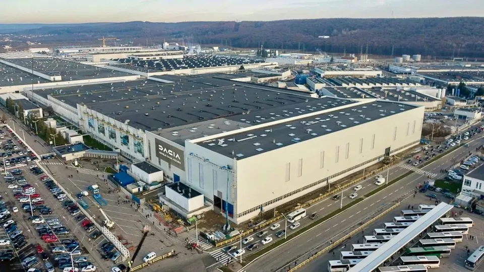 O vedere aeriană prezintă un complex industrial extins cu clădiri mari de culoare deschisă, parcuri de mașini și drumuri în apropiere.