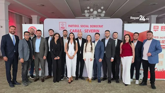Un grup de oameni stă în picioare în fața unui panou alb cu text colorat, purtând haine formale și casual.