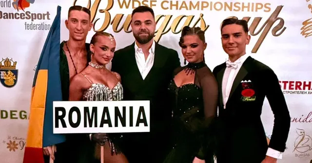 Patru persoane stau în picioare în fața unui panou alb, două femei purtând rochii de seară și doi bărbați în costume elegante.
