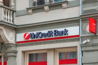O fațadă de clădire prezintă un panou alb cu inscripția UniCredit Bank scrisă cu litere albastre și un logo roșu circular.
