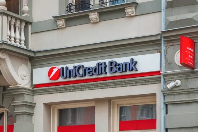O fațadă de clădire prezintă un panou alb cu inscripția UniCredit Bank scrisă cu litere albastre și un logo roșu circular.