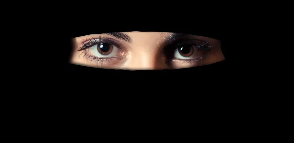 O pereche de ochi umani este vizibilă printr-o deschidere îngustă într-un material negru.