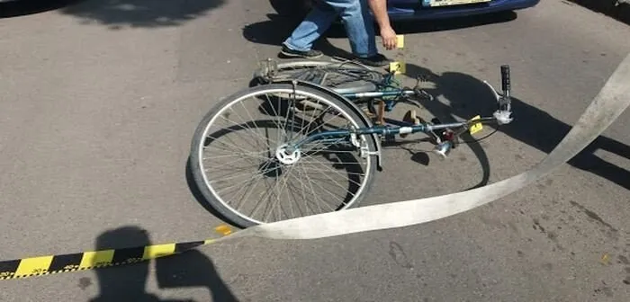 Un bicicletă de culoare închisă este întinsă pe asfalt lângă o bandă de delimitare galbenă și neagră.