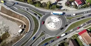 O vedere aeriană prezintă un sens giratoriu cu mai multe benzi de circulație, vehicule colorate și margini marcate cu linii albe pe asfaltul gri.