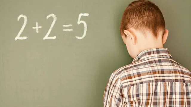 Un copil cu o cămașă în carouri stă cu spatele în fața unei table verzi pe care este scris 2+2=5 cu cretă albă.