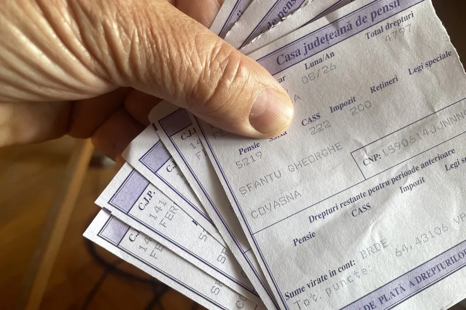 O mână ține mai multe documente de plăți emise de Casa Județeană de Pensii, cu textul și datele clar vizibile pe ele.