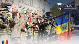 O linie de militari în uniforme de camuflaj stă în picioare, purtând căciuli și ținând un steag tricolor cu embleme pe un stârf lung.