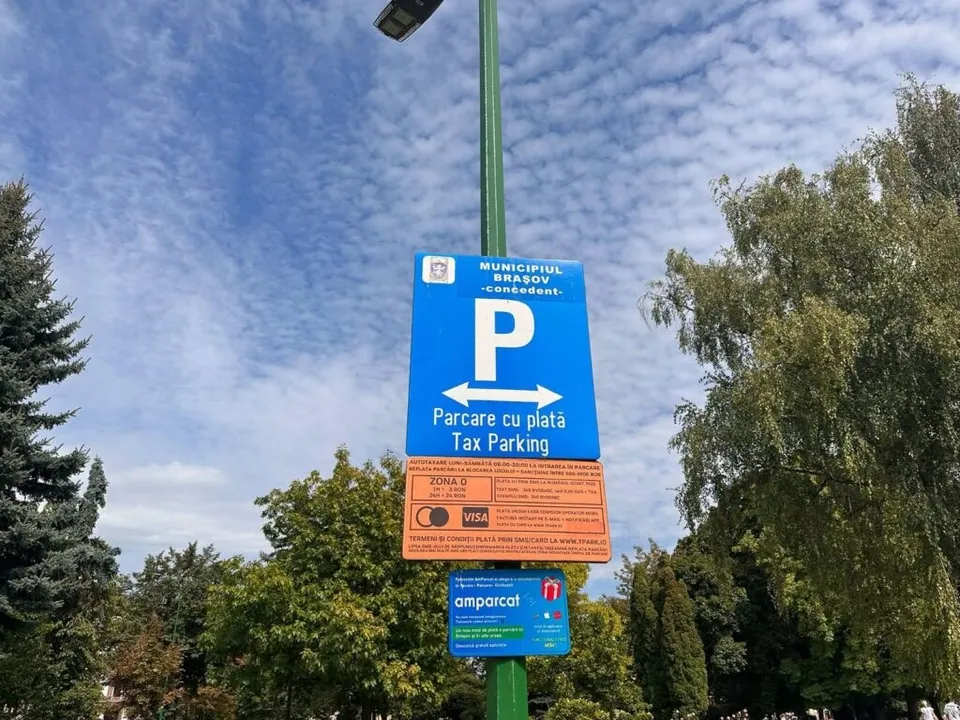 Un semn albastru cu litera P albă și textul parcare cu plată este montat pe un stâlp verde sub un cer cu nori subțiri.