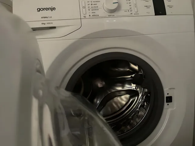 O mașină de spălat albă cu ușa deschisă dezvăluie tamburul metalic strălucitor în interior.
