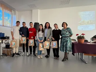 Opt persoane stau în rând într-o încăpere, câțiva dintre ei țin în mâini pliante colorate în fața lor.