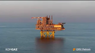 O platformă petrolieră de culoare galbenă este situată pe o suprafață de apă sub un cer de seară.