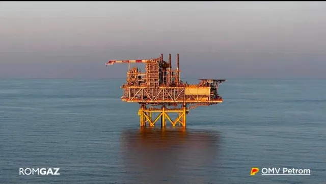 O platformă petrolieră de culoare galbenă este situată pe o suprafață de apă sub un cer de seară.