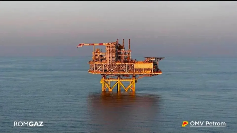 O platformă petrolieră de culoare galbenă este situată pe o suprafață de apă sub un cer de seară.
