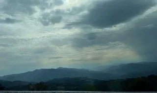 Un cer acoperit de nori gri și albi deasupra unui peisaj format din dealuri și munți întinși sub o lumină difuză.