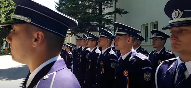O serie de bărbați în uniforme de serviciu și căciuli de poliție stau aliniați în exterior, în fața unei clădiri și a unui copac.