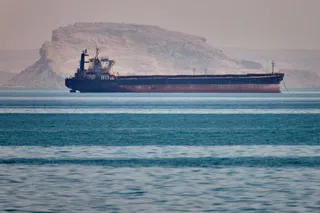 Un vapor mare de mare navigă pe o suprafață de apă cu un deal împădurit în fundal.