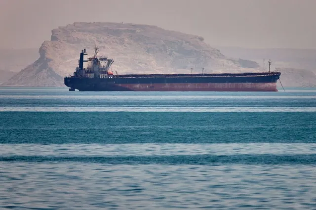 Un vapor mare de mare navigă pe o suprafață de apă cu un deal împădurit în fundal.