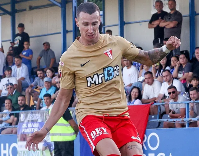 Un bărbat cu tricou auriu și pantaloni scurți roșii aleargă pe un teren de fotbal în fața unor spectatori așezați pe tribune.