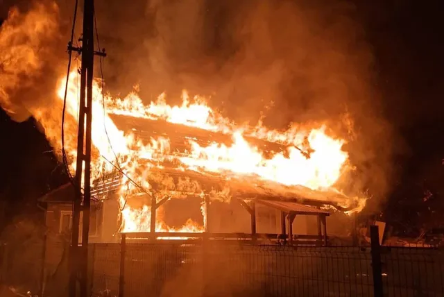 Flăcări mari și fum dens acoperă acoperișul unei clădiri într-un cadru nocturn, lângă un stâlp de utilități.