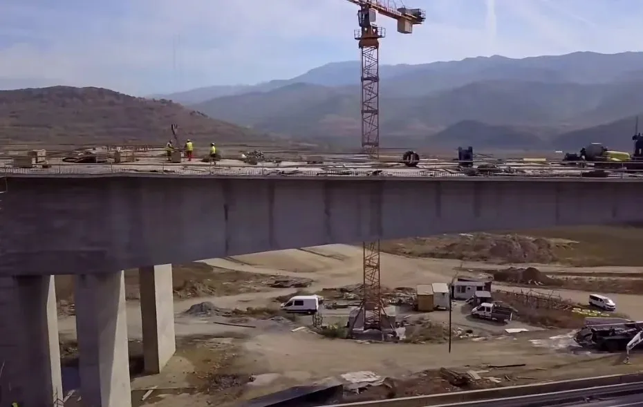 O platformă de beton susținută de piloni se află într-un șantier cu o macara de construcție și câteva vehicule parcate pe terenul din spate.