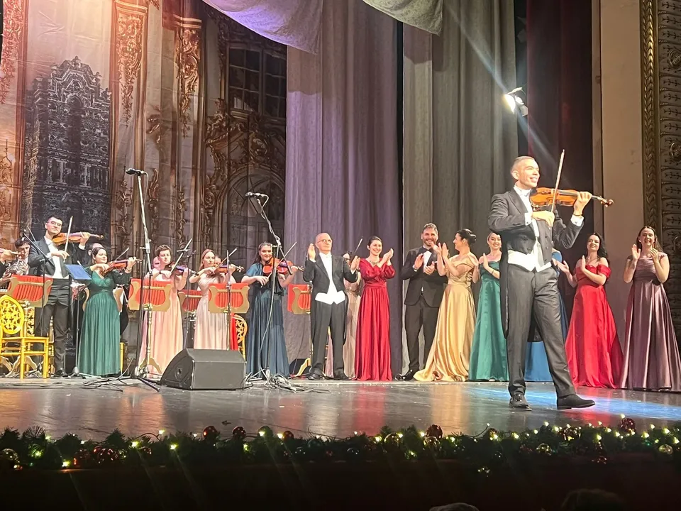 Un grup de muzicieni și artiști în haine de seară stau pe o scenă de teatru în fața unui decor pictat.