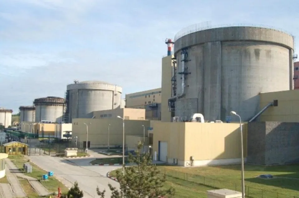 Mai multe structuri cilindrice de beton și clădiri industriale de culoare deschisă sunt situate pe un teren cu vegetație sub un cer înzăpezit.