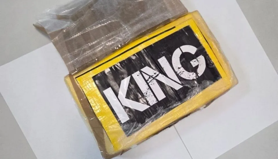 Un pachet dreptunghiular învelit în folie de plastic, cu un etichetă galbenă pe care scrie textul alb "KING" pe un fundal negru, este așezat pe o suprafață albă.