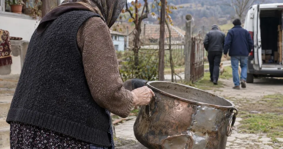 O persoană purtând un vest negru și o bluză maro ține un cazan metalic mare cu mâner negru într-un decor exterior.