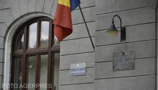 O parte dintr-o fațadă gri cu o fereastră arcuită, un steag românesc și o placă cu inscripția Curtea de Conturi.