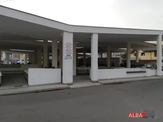 O structură deschisă cu coloane albe susține un acoperiș plat deasupra unor spații comerciale cu mese de prezentare albe.